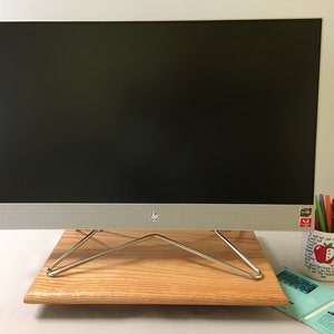 May include: A silver computer monitor with a black screen is on a wooden stand with a metal frame. The monitor is sitting on a wooden surface. There is a mug with a red apple and the text "I will tell you in class, you will never know because I am the teacher" on the right side of the image.