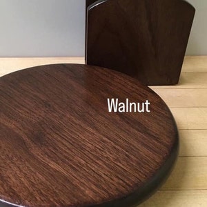 May include: A round wooden coaster in a dark walnut stain. The coaster has a slightly raised edge.