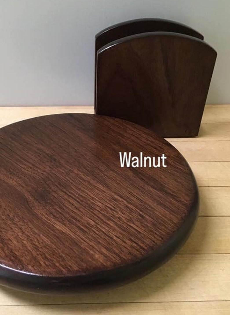 May include: A round wooden coaster in a dark walnut stain. The coaster has a slightly raised edge.