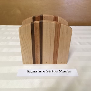 May include: Wooden napkin holder with a striped design in shades of brown and maple. The holder is labeled "Signature Stripe Maple".