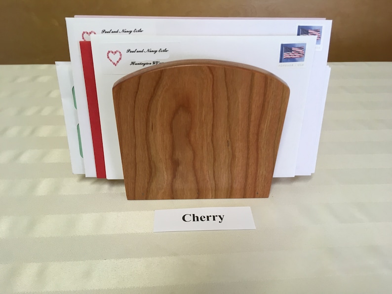 May include: A wooden letter holder made of cherry wood. The holder is holding several envelopes with stamps. The label below the holder reads "Cherry".
