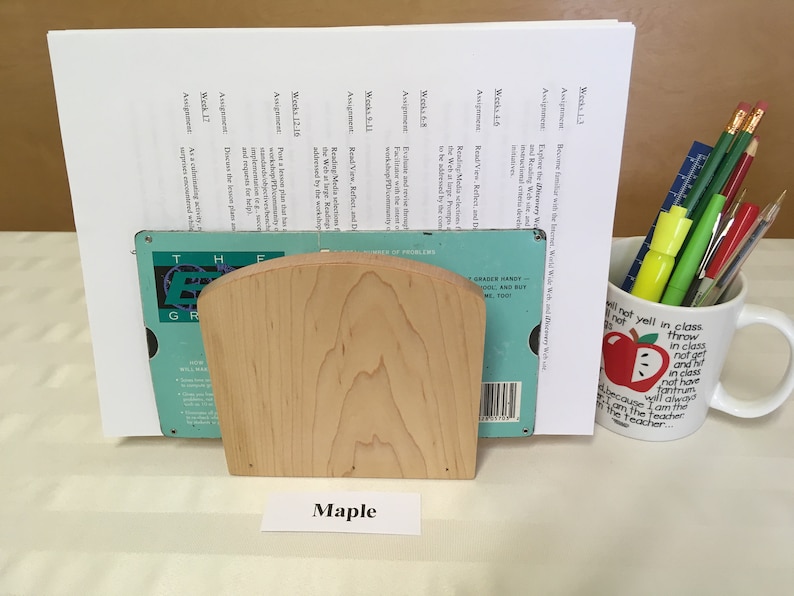 May include: A wooden bookend with a curved top and a label that reads "Maple". The bookend is holding a blue and green book with a white label that reads "The Essential Grammar in Use".