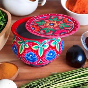 Puede incluir: Un cuenco de cerámica pintado a mano con tapa a juego. El cuenco es rojo con diseños florales en azul, verde y rosa. La tapa redonda tiene un diseño floral. El cuenco está rodeado de ingredientes.