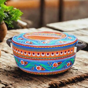 Könnte beinhalten: Eine runde, farbenfrohe Servierschüssel mit Deckel. Die Schüssel hat ein lebendiges Design mit blauen, orangefarbenen und weißen Blumenmustern. Sie hat zwei graue Griffe und steht auf einer Holzoberfläche. Ideal zum Servieren von Speisen.