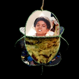 May include: A green and gold Christmas ornament featuring a photo of a young boy with the text "Randy" and "J5" on the ornament.