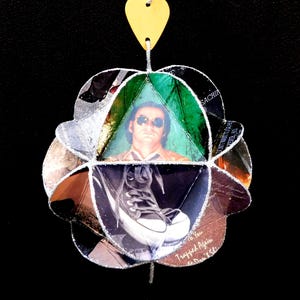 May include: A handmade, multi-faceted ornament with a yellow top. The ornament features images of a person wearing sunglasses and a pair of black and white sneakers. The ornament is made of various materials and has a unique, artistic design.