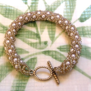 May include: A delicate pearl and gold bracelet with a toggle clasp. The bracelet is made of small, white pearls and gold beads.