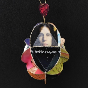 May include: A handmade pendant featuring a portrait of a person, with the text "todd rundgren" visible. The pendant is made of layered, colorful paper and has a red heart-shaped charm at the top, suspended by a gold chain.