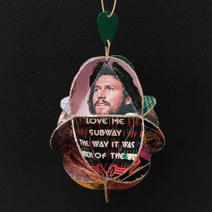 May include: A handmade ornament featuring a portrait of a man and the text "LOVE ME SUBWAY THE WAY IT WAS REN OF THE WO". The ornament has a gold string and a green heart-shaped top.