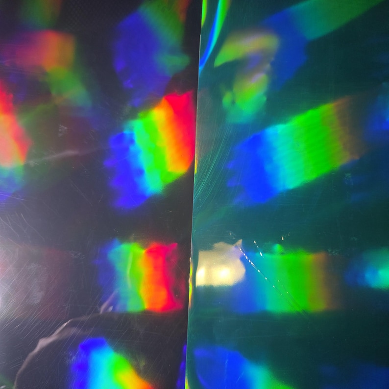 May include: Abstract image of iridescent material with a spectrum of colors. The surface reflects light, displaying bands of red, orange, yellow, green, blue, and purple. The material appears to be slightly textured, with subtle imperfections.
