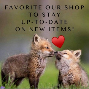 May include: Two fox kits, one brown and one tan, touch noses in a grassy field. A red heart graphic is above them. Text at the top reads, "FAVORITE OUR SHOP TO STAY UP-TO-DATE ON NEW ITEMS!"