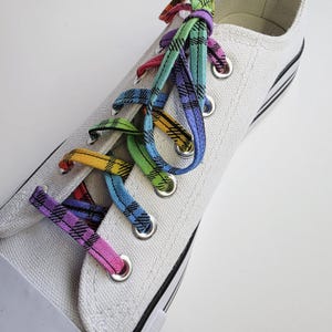 May include: White canvas sneakers with rainbow plaid shoelaces tied in a criss-cross pattern.