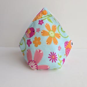 May include: A light blue fabric pouch featuring a floral and bird pattern. The design includes orange, pink, and green flowers, along with a bird and an owl. The pouch is a unique shape, with a button closure.