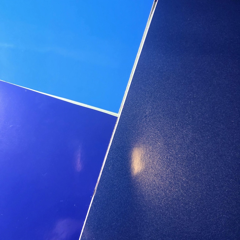 May include: Abstract composition featuring three distinct blue surfaces. The top section is a light blue, the bottom left is a darker blue, and the right is a textured, deep navy blue. The surfaces are separated by thin white lines.