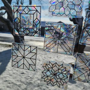 May include: A set of eight iridescent, geometric window clings with black outlines. The clings feature various patterns, including stars, diamonds, and squares.