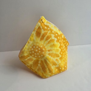 Puede incluir: Una bolsa de tela amarilla con un diseño de girasol. La bolsa está hecha de tela amarilla brillante con un patrón de puntos blancos. Un botón amarillo asegura la solapa superior. La bolsa probablemente se usa para guardar cosas.