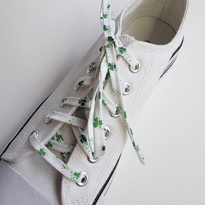May include: White canvas sneakers with green shamrock patterned shoelaces. The laces are tied in a criss-cross pattern.