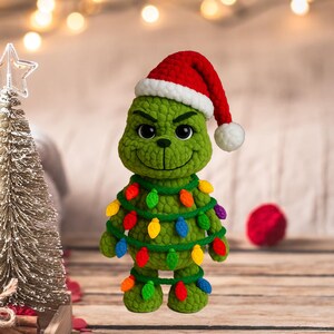 May include: A handmade green crochet Grinch figure wearing a red Santa hat with a white trim and a white pom-pom. The Grinch is adorned with a string of colorful Christmas lights, perfect for holiday decor.