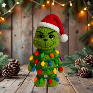 May include: A green crocheted Grinch doll wearing a red and white Santa hat and a string of colorful Christmas lights. The Grinch has a smiling face and is standing on a wooden surface, with pinecones and Christmas tree branches in the background.