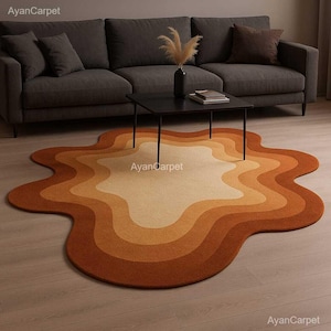 May include: A large, abstract, multi-colored rug with a wavy, organic shape. The rug has a light beige center with concentric rings of orange, brown, and rust.