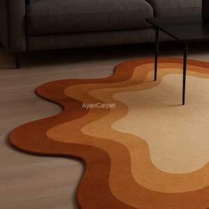 May include: A wavy, abstract area rug with a multi-colored design in shades of brown, orange, and beige. The rug is made of a soft, plush material and has a unique, organic shape.