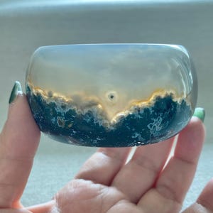 May include: A polished, wide bangle bracelet crafted from translucent agate stone. The stone features a distinct horizontal color gradient, transitioning from a deep, mossy forest green at the base to a clear, pale gray at the top edge.