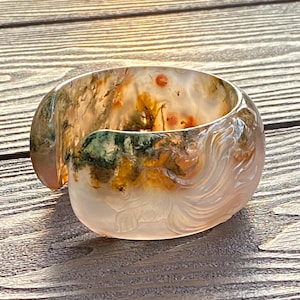 以下が含まれることがあります： 半透明で彫刻された宝石のブレスレット。ブレスレットは、緑、オレンジ、白など、さまざまな色を特徴としています。ブレスレットは滑らかで磨かれた仕上げで、直径は約6.35cmです。