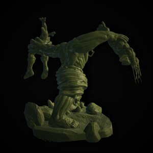 May include: A green figurine of a muscular monster holding a smaller figure. The monster is posed on a rocky base with several stones. The monster's arm is outstretched, and it has a menacing expression.