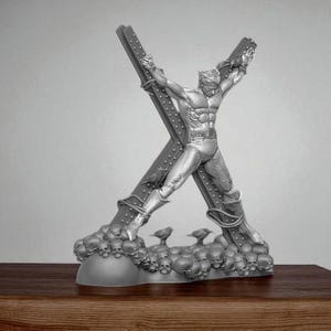 May include: A silver-colored sculpture of a superhero figure attached to a large X-shaped structure. The base of the sculpture is adorned with skulls and small bird figures. The sculpture is displayed on a wooden surface.