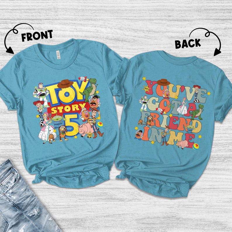 K&ouml;nnte beinhalten: Zwei hellblaue T-Shirts mit Toy Story-Designs. Das vordere Shirt zeigt "Toy Story 5" mit Charakteren. Das hintere Shirt hat "You've Got a Friend in Me" mit Charakteren. Ein farbenfrohes Design f&uuml;r Fans des Animationsfilms.