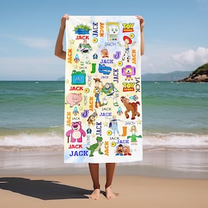 May include: A white beach towel featuring colorful cartoon characters from the Toy Story movie. The towel has a repeating pattern of characters, stars, rockets, and the word "JACK". The Toy Story logo is also visible.