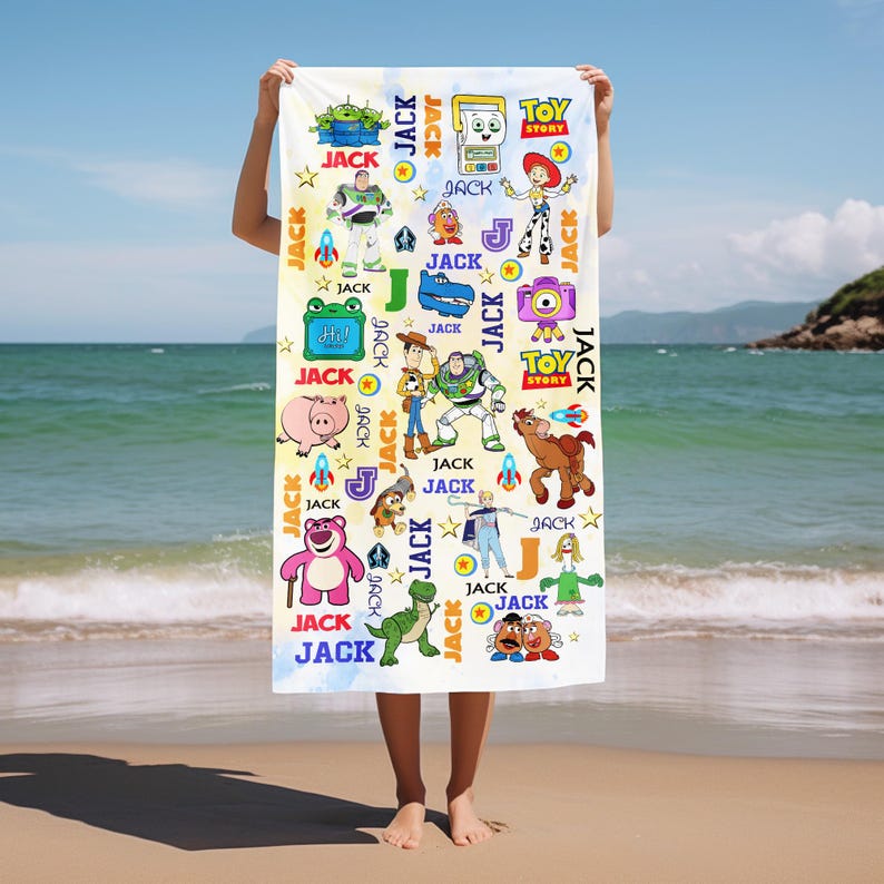 May include: A white beach towel featuring colorful cartoon characters from the Toy Story movie. The towel has a repeating pattern of characters, stars, rockets, and the word "JACK". The Toy Story logo is also visible.