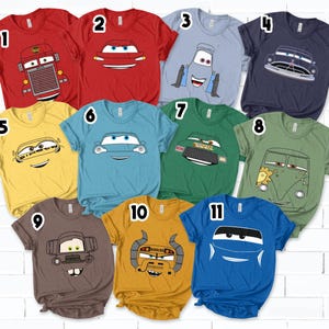 May include: A collection of eleven short-sleeved t-shirts in various colors, each featuring a cartoon car design. The shirts are red, yellow, blue, green, and brown. The car designs vary, with different expressions and styles.