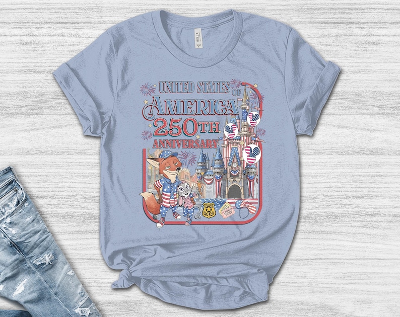 Puede incluir: Camiseta azul claro con un gr&aacute;fico colorido que celebra el 250 aniversario de los Estados Unidos de Am&eacute;rica. El dise&ntilde;o incluye personajes de dibujos animados, un castillo y elementos patri&oacute;ticos.
