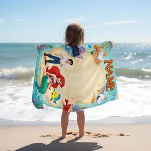May include: A beach towel with a vibrant illustration of characters from a popular animated film. The design includes a mermaid, a prince, and other sea creatures. The word "NAME" is printed on the towel.