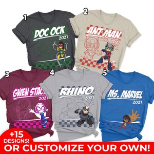 Pode incluir: Cinco camisetas de manga curta em cinza escuro, bege, bord&ocirc;, cinza e azul, cada uma com um personagem da Marvel, o nome, o ano 2021 e um padr&atilde;o xadrez. Um emblema circular vermelho no canto diz +15 DESIGNS!