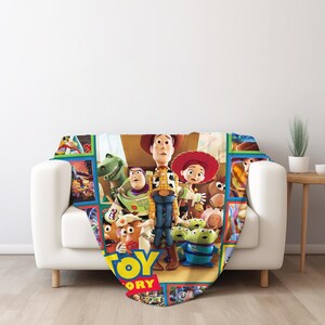 May include: A soft throw blanket featuring a colorful graphic print of characters from the movie Toy Story, including Woody, Buzz Lightyear, Jessie, Rex, and the Aliens, with the Toy Story logo prominently displayed at the bottom of the design.