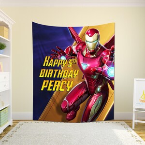 Puede incluir: Un tapiz de Iron Man rojo y dorado con el texto "Happy 5th Birthday Percy". El superh&eacute;roe est&aacute; en una pose din&aacute;mica sobre un fondo azul y dorado. Ideal para una fiesta de cumplea&ntilde;os infantil o la decoraci&oacute;n de un dormitorio.