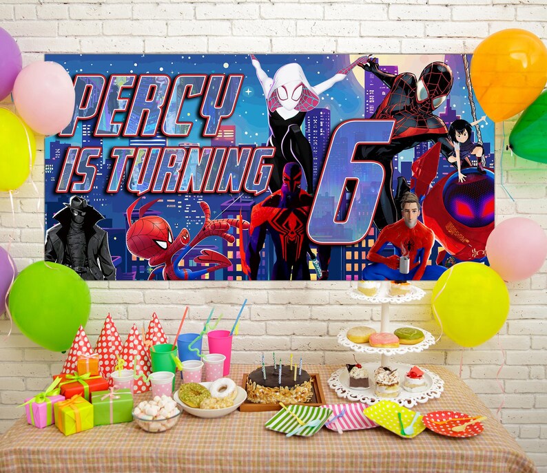 May include: A rectangular birthday banner featuring Spider-Man characters and the text Percy is turning 6, displayed above a table with party supplies including colorful balloons, gift boxes, party hats, and a chocolate cake on a stand.