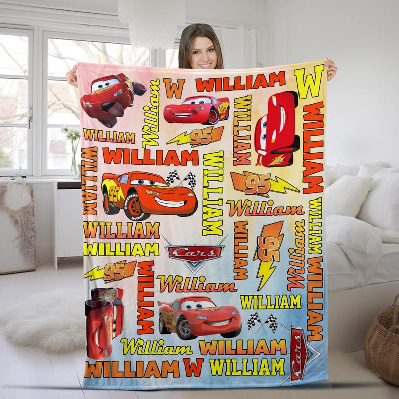 Puede incluir: Una colorida manta con el personaje Rayo McQueen de la pel&iacute;cula Cars. La manta tiene un fondo degradado e incluye el nombre "William" y el n&uacute;mero "95" en varios dise&ntilde;os. La manta es una vibrante mezcla de rojo, amarillo y azul.