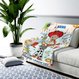 May include: A soft throw blanket featuring a cartoon cowgirl with red hair playing a guitar, surrounded by western-themed icons like boots, stars, and cacti. The text "NAME" and "KNEW IT, I KNEW YOU" are printed in blue on a light blue background.