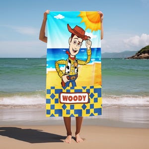 May include: A rectangular beach towel featuring a cartoon illustration of the character Woody from Toy Story wearing a brown cowboy hat, yellow plaid shirt, and cow-print vest. The bottom section has a yellow and blue geometric pattern with a white rectangular label containing the red text WOODY.