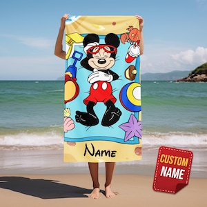 May include: A beach towel featuring Mickey Mouse in a beach scene. Mickey is wearing sunglasses and red shorts, surrounded by beach toys and a starfish. The towel has a blue background with the word "Name" printed on it.