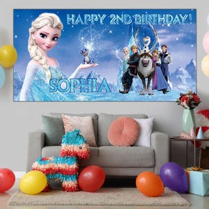 Puede incluir: Una pancarta de cumplea&ntilde;os con el texto "HAPPY 2ND BIRTHDAY!" y el nombre "SOPHIA" presenta personajes de la pel&iacute;cula Frozen. La escena incluye a Elsa, Anna, Olaf, Kristoff y Sven. Globos y decoraciones de fiesta completan el ambiente festivo.
