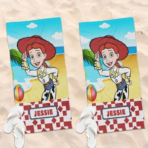 May include: Two rectangular beach towels featuring a cartoon cowgirl with red hair, a red hat, and a white and yellow shirt. The background shows a beach scene with a colorful ball. Below, a red and white geometric pattern contains the name JESSIE.