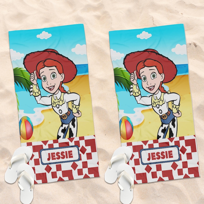 May include: Two rectangular beach towels featuring a cartoon cowgirl with red hair, a red hat, and a white and yellow shirt. The background shows a beach scene with a colorful ball. Below, a red and white geometric pattern contains the name JESSIE.