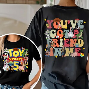 K&ouml;nnte beinhalten: Schwarzes T-Shirt mit einem farbenfrohen Grafikdesign aus dem Film "Toy Story". Das Design auf der Vorderseite zeigt "Toy Story 5" mit verschiedenen Charakteren. Auf der R&uuml;ckseite steht "You've Got A Friend In Me".
