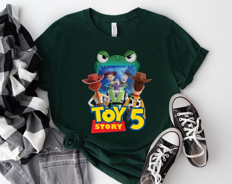 May include: Dark green t-shirt featuring a colorful graphic of characters from the movie Toy Story 5. The graphic includes Woody, Buzz Lightyear, and Jessie. The text "TOY STORY 5" is in yellow and red. Black canvas sneakers are next to the shirt.