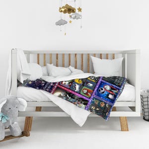 May include: A colorful throw blanket featuring a patchwork design with images of characters from The Nightmare Before Christmas. The blanket is draped over a white crib with a plush elephant toy and a mobile hanging above.