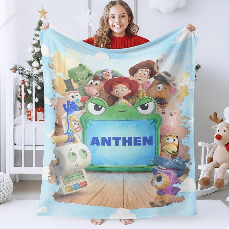 May include: A soft fleece blanket featuring a colorful collage of Toy Story characters surrounding a central green frog-shaped frame. The name ANTHEN is printed in bold blue capital letters inside the frame, set against a light blue sky background.